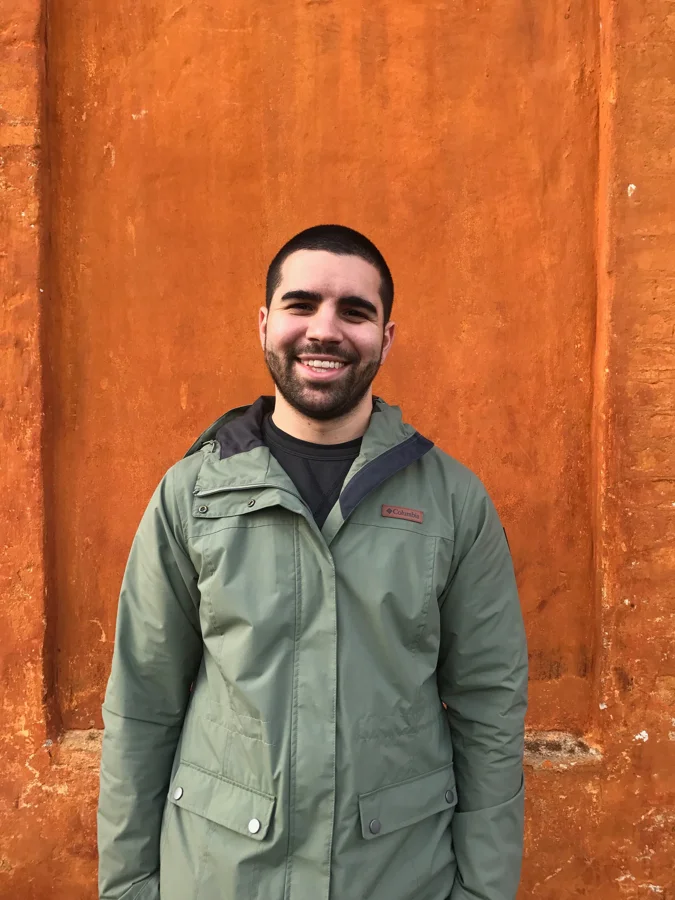 Zach smiling in front of an orange wall